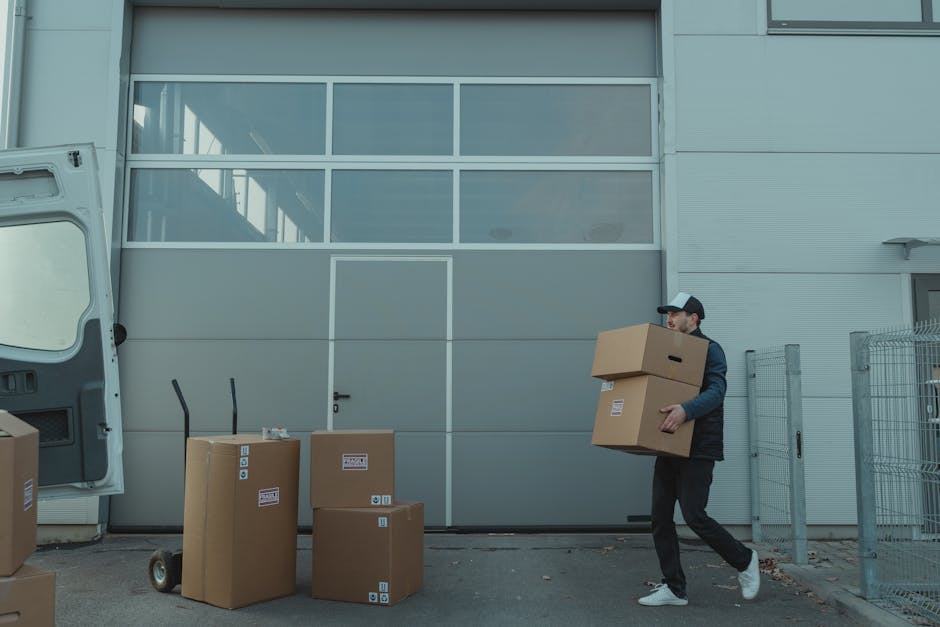 A collection of moving boxes made of kraft cardboard, labeled with black marker handwriting. The top box, positioned inside a home or storage area, has the word 'STUFF' written on it along with a smil